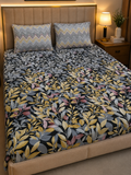 A bed dressed in a dark floral-patterned duvet cover with yellow, gray, and pink leaves, styled with two matching chevron-patterned pillows in a warm bedroom setting.