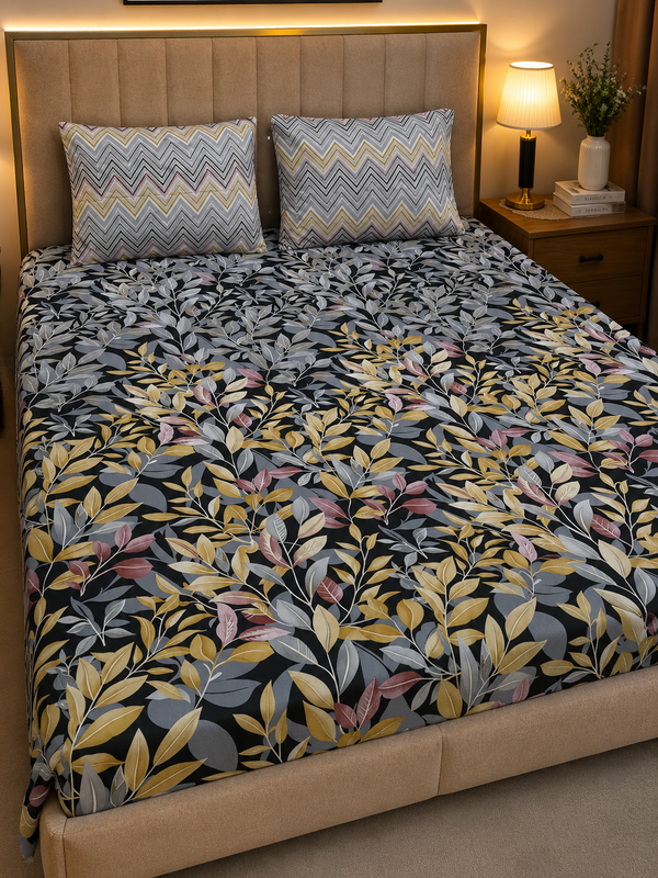 A bed dressed in a dark floral-patterned duvet cover with yellow, gray, and pink leaves, styled with two matching chevron-patterned pillows in a warm bedroom setting.