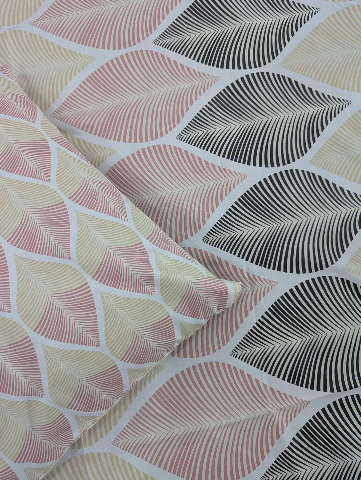 A close-up of patterned fabric with a repeating leaf design in blush pink, cream, and black on a white base, with a folded section showing the texture and color mix.