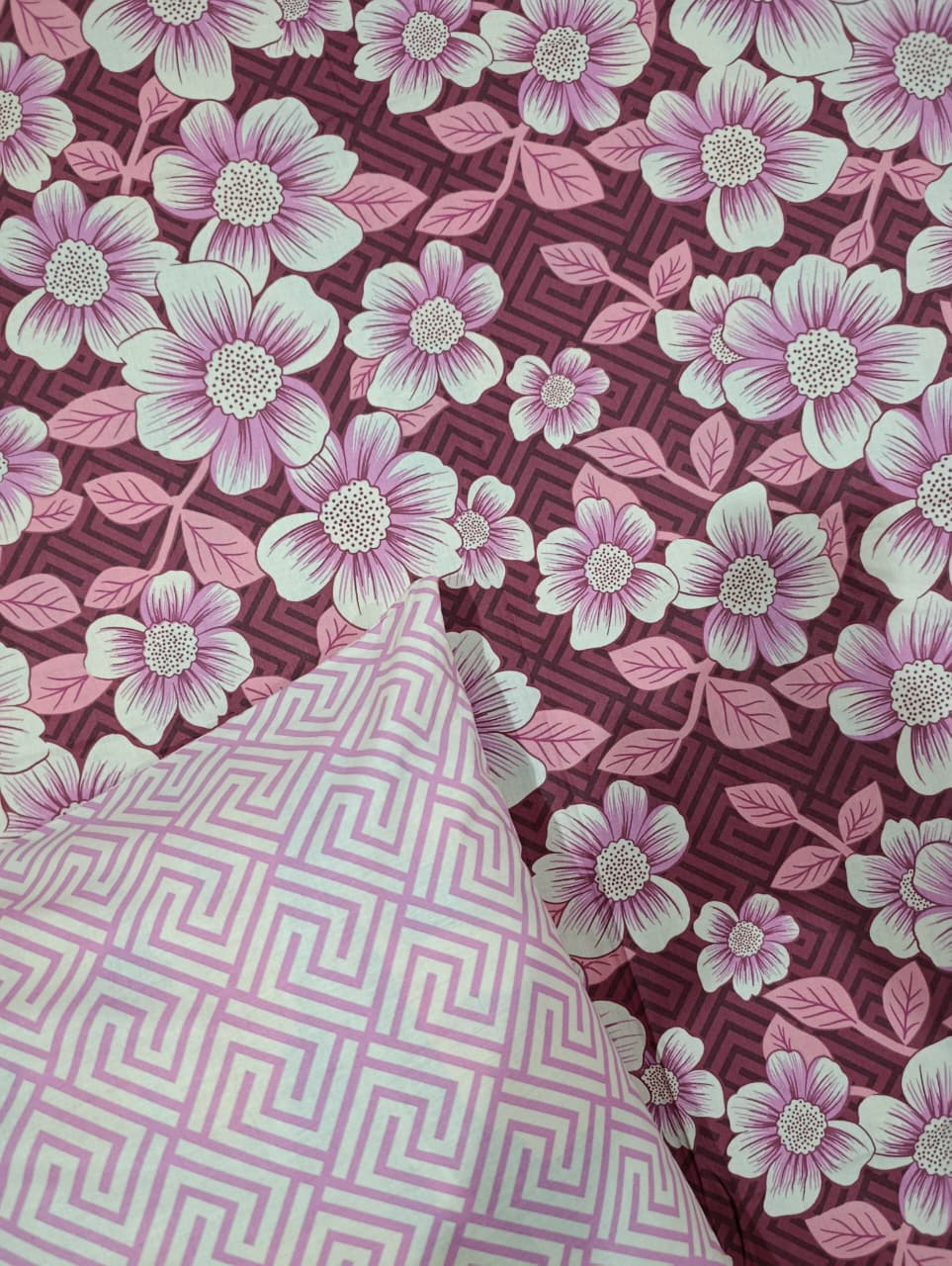 A close-up of patterned fabric with a large pink and white floral print over a dark burgundy geometric background, plus a folded section showing a matching pink and white geometric pattern.