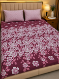 A bed dressed in a dark burgundy floral quilt with pink and white cherry blossom patterns, styled with two matching pink pillows in a bedroom setting.