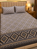 A neatly made bed with a patterned bedding set in a warm bedroom. The set includes a light gray duvet cover and two matching pillowcases, both featuring a repeating geometric diamond motif in beige, brown, and gray.
