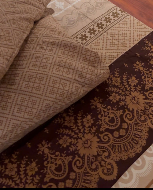 A close-up of patterned bedding or fabric pieces layered together, showing a beige geometric textile, a cream floral border section, and a dark brown panel with ornate gold paisley and floral motifs.