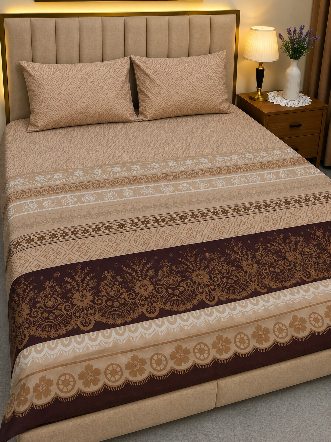 A neatly made bed with a beige and brown patterned bedding set, featuring a decorative floral border runner and matching pillows, shown in a bedroom setting with a nightstand and lamp.