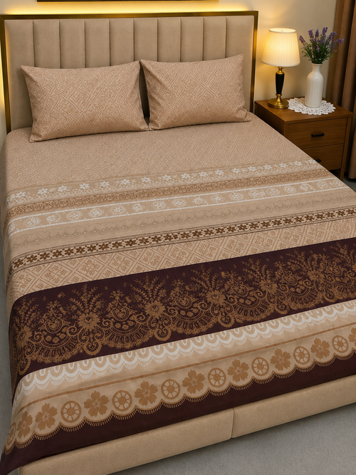 A neatly made bed with a beige and brown patterned bedding set, featuring a decorative floral border runner and matching pillows, shown in a bedroom setting with a nightstand and lamp.