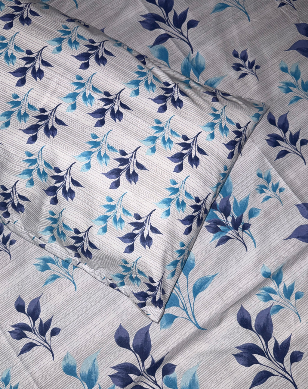 A close-up of a textured fabric featuring a repeating floral pattern with dark navy blue and light blue leaves on a light gray background.