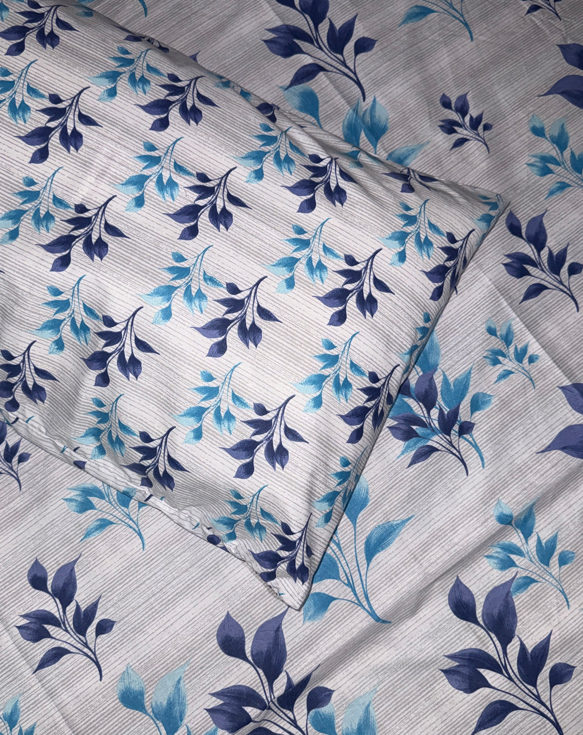 A close-up of a textured fabric featuring a repeating floral pattern with dark navy blue and light blue leaves on a light gray background.