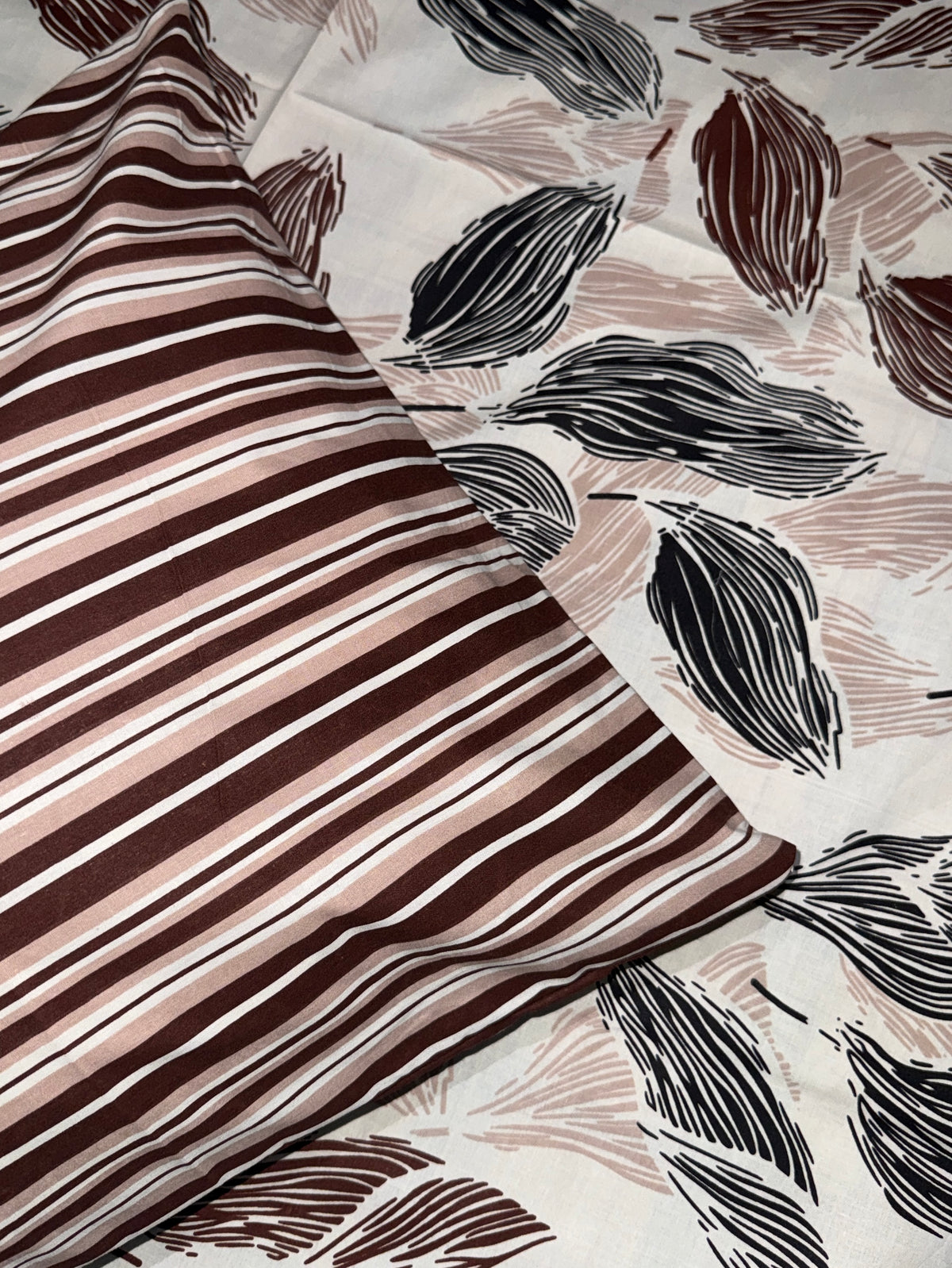 A close-up of a bedding set featuring a striped pillowcase and a matching duvet cover. The pillowcase has diagonal stripes in dark brown, dusty rose, and white.