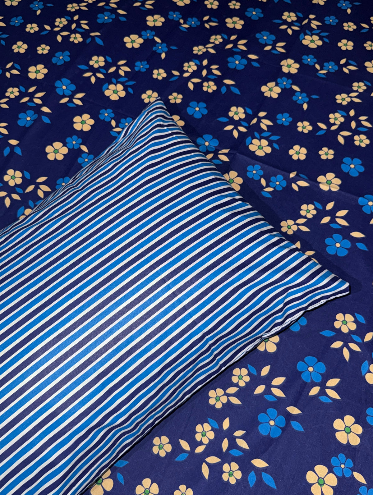 A blue and white striped pillowcase placed on top of a navy blue bedspread with a yellow and blue floral pattern.