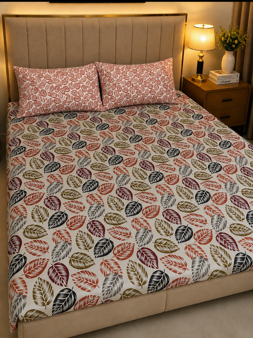 A bed dressed in a patterned duvet cover and matching pillowcases featuring a repeating leaf motif in muted red, olive green, gray, and brown on a cream background, shown in a warmly lit bedroom setting.