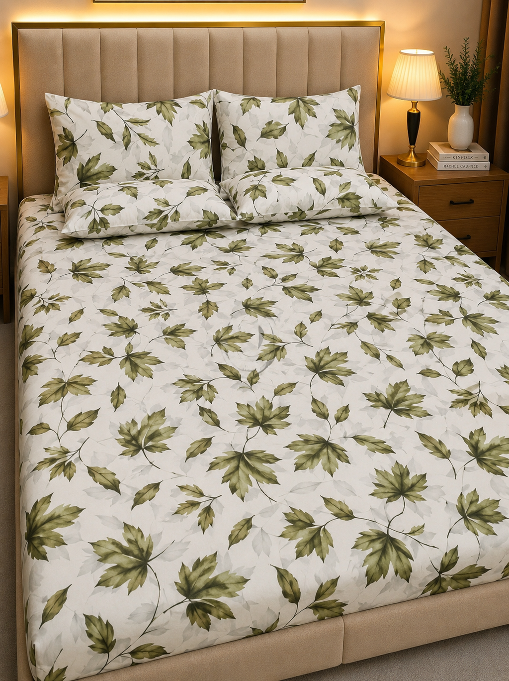 A bed dressed in a white bedding set with an all-over green leaf pattern, including a duvet cover and matching pillowcases, styled in a warm, modern bedroom setting with a padded headboard and bedside lamp.