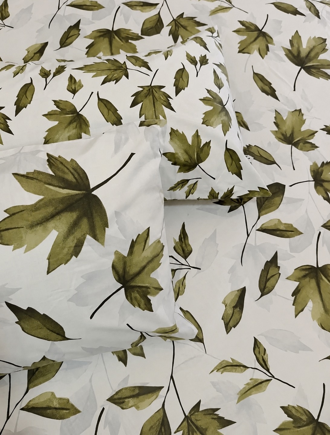 White bedding set with a repeating pattern of olive green maple leaves and dark stems, including a flat sheet and two pillowcases.