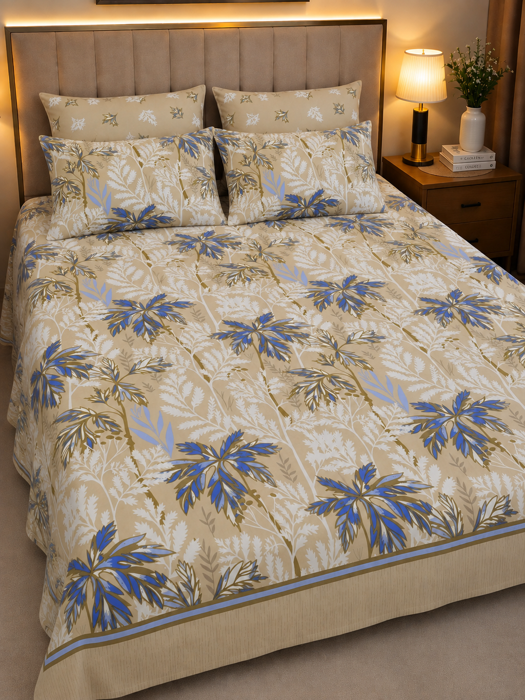 A made bed in a bedroom setting featuring a beige quilted comforter and matching pillow shams with a blue and white tropical palm leaf pattern.