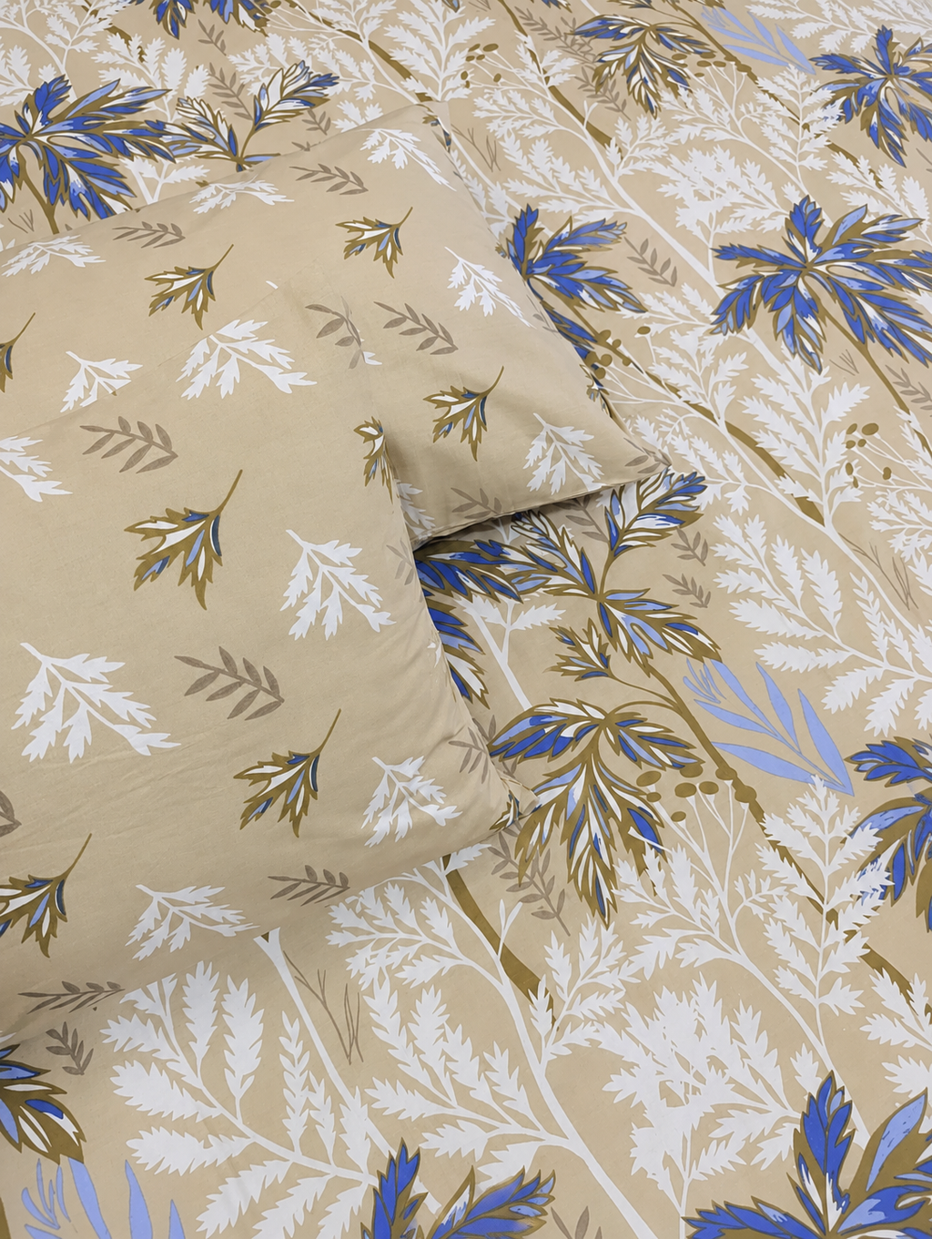 A close-up of a beige bedding set featuring a botanical leaf pattern in blue, white, and olive green, with a matching pillowcase resting on top.