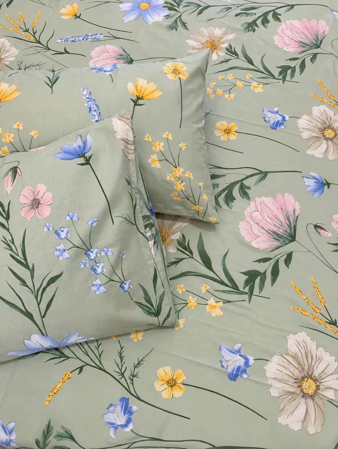A floral bedding set featuring a sage green duvet cover and matching pillowcases with a vibrant print of pink, yellow, and blue wildflowers and green foliage.