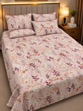 A bed dressed in a light pink floral bedding set with matching pillowcases, shown in a warmly lit bedroom setting with a wooden headboard, bedside lamp, and nightstand.