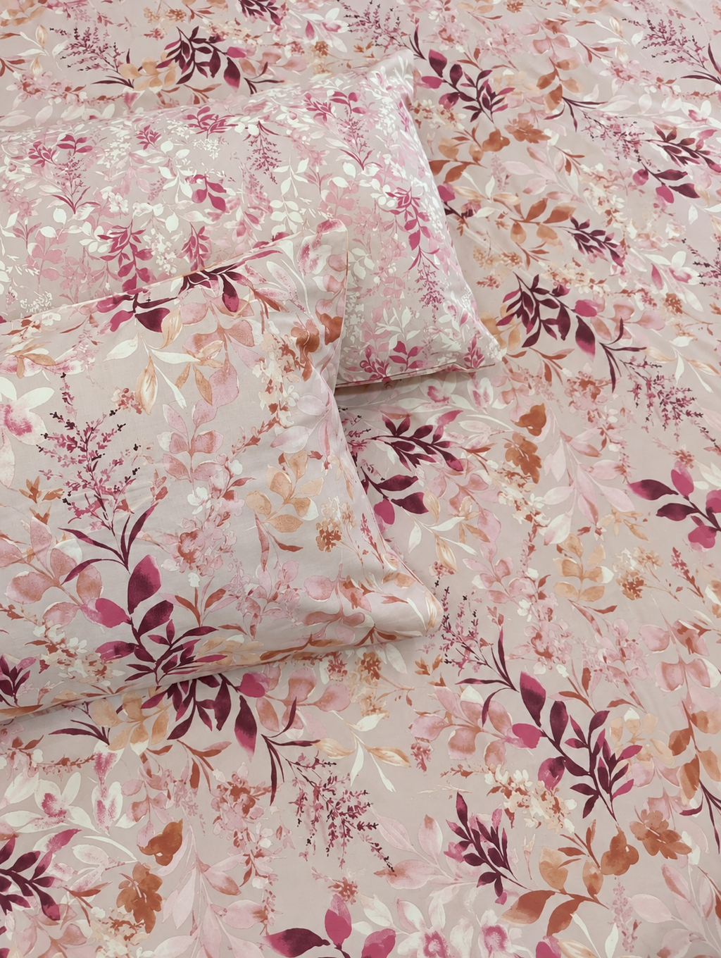 A close-up of a floral bedding set featuring a duvet cover and matching pillowcases with a delicate pink, burgundy, and beige botanical pattern.