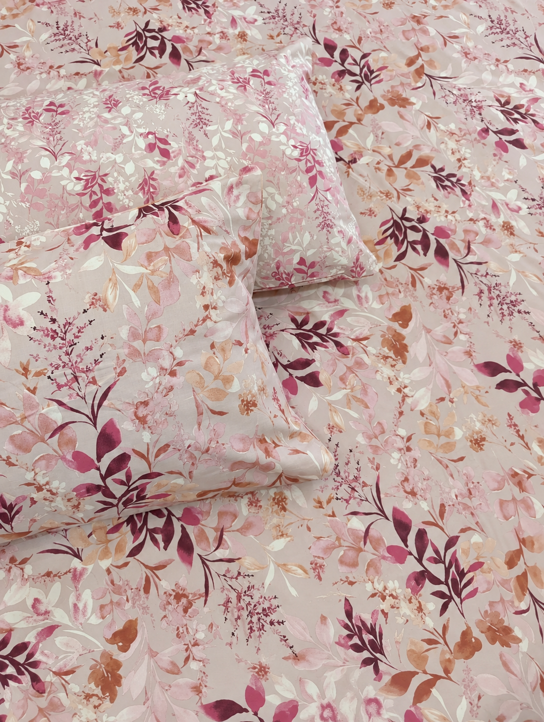 A close-up of a floral bedding set featuring a duvet cover and matching pillowcases with a delicate pink, burgundy, and beige botanical pattern.